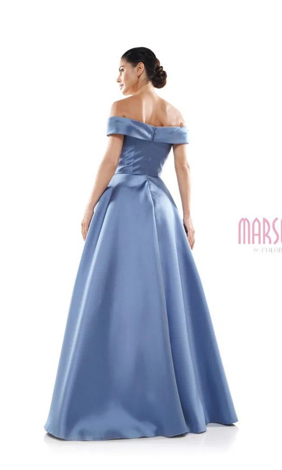 A woman stands with her back to the camera against a white background, wearing the Marsoni MV1008—a floor-length, off-the-shoulder formal dress in satin blue with beaded applique.